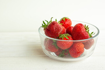 Strawberries in a glass bowl on a white wooden background.
