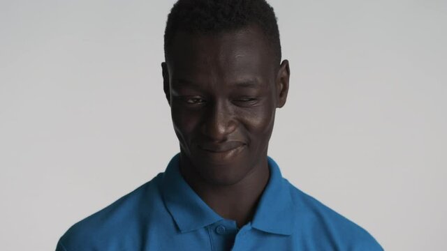 Portrait of attractive African American guy slyly looking around and laughing on camera over gray background. Gamine expression