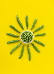 Fresh green peas on a bright yellow background. Sunny pattern of pods and peeled peas. Fun food. Summer minimal concept.