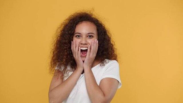Side profile view young african woman girl 20s in white t-shirt posing isolated on yellow background studio. People lifestyle concept Look camera turn round surprised shocked say wow put hands on face