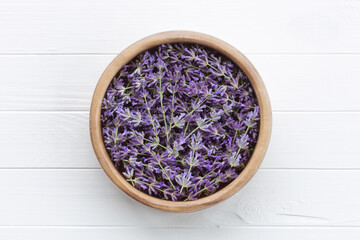 Obraz na płótnie Canvas Lavender flowers in a wooden bowl on a white wooden table. Fragrant flowers for making essences, cooking, medical and cosmetology.