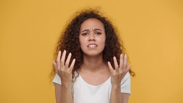 Sad upset young african woman girl in white t-shirt posing isolated on yellow background studio. People sincere emotions lifestyle concept. Looking camera crying waving hands ask why sadness problem