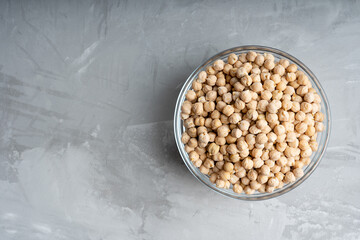 Glass bowl full of uncooked raw chickpea standing on concrete surface at the right. Image with copy...