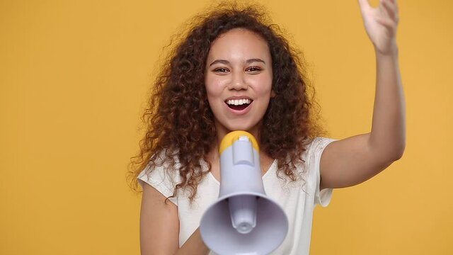 Fun crazy young african american woman girl in white t-shirt posing isolated on yellow background studio. People lifestyle concept. Looking camera scream in megaphone announces discounts sale Hurry up