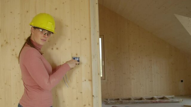 SLOW MOTION CLOSE UP, COPY SPACE, PORTRAIT: Young Female Electrician Screws An Outlet Frame Onto A Wooden Wall In Place Of A Light Switch And Turns Toward The Camera. Woman Installs An Electric Outlet