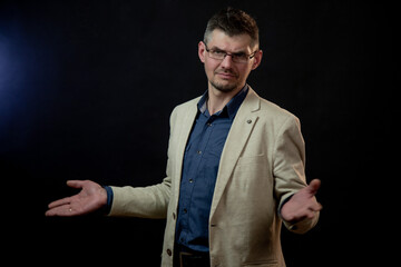 actor in glasses and classic suit spreads arms in amazement posing for photo shoot against black...
