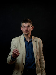angry actor with tree-day stubble in glasses shows fist on dark studio stage under bright electric...