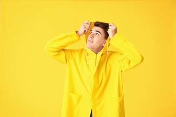 Handsome young man in raincoat on color background