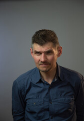 mature actor with bad vision without glasses looks attentively posing for camera against grey studio wall close view