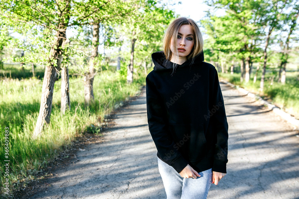 Wall mural blonde woman in black hoodie posing in the park, mock up clothes for printing