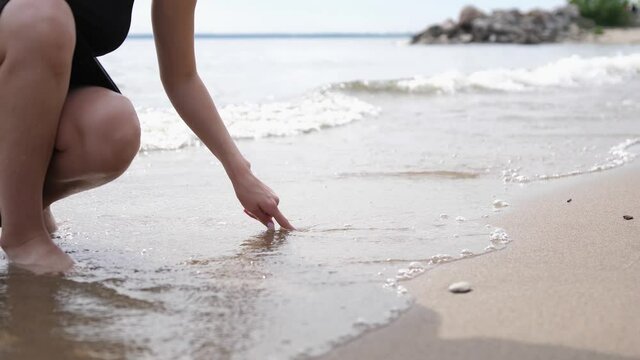 Woman hand drawing heart on sand by the beach and wave clear off the heart on the shore