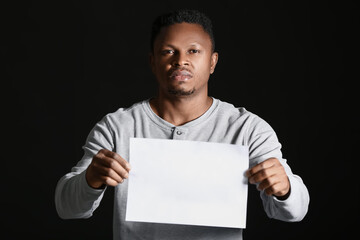 Sad African-American man with poster on dark background. Stop racism