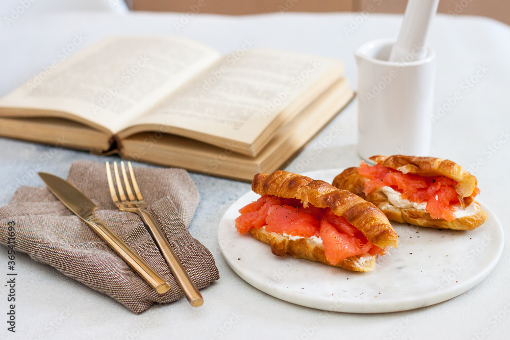 Poster delicious breakfast with croissant, smoked salmon, cheese and pepper on white plate. opened old book