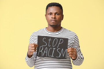 Sad African-American man with poster on color background. Stop racism