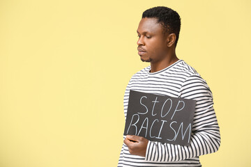 Sad African-American man with poster on color background. Stop racism