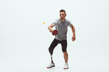 Fototapeta na wymiar Athlete with disabilities or amputee isolated on white studio background. Professional male table tennis player with leg prosthesis training in studio. Disabled sport and healthy lifestyle concept.