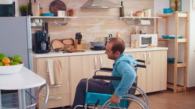 Disabled man in wheelchair helping wife in kitchen. Opening refrigerator. Guy with paralysis handicap disability handicapped difficulties getting help for mobility from love and relationship