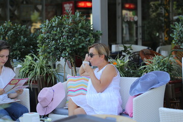 two girls are sitting in a cafe drinking coffee and taking selfies