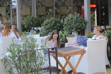 two girls are sitting in a cafe drinking coffee and taking selfies