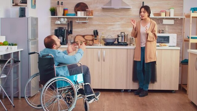 Wife screaming in kitchen to her disabled man in wheelchair while having a disagreement. Guy with paralysis handicap disability handicapped difficulties getting help for mobility from love and
