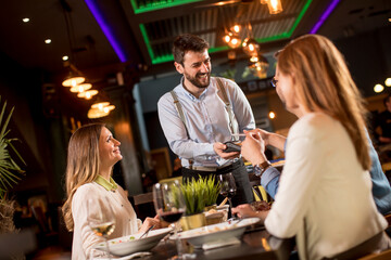 Young man paying with contactless credit card in the restaurant