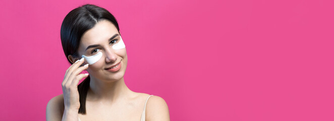 Close up portrait of pretty attractive girl with naked shoulders using patches under eyes. Standing over pink background.