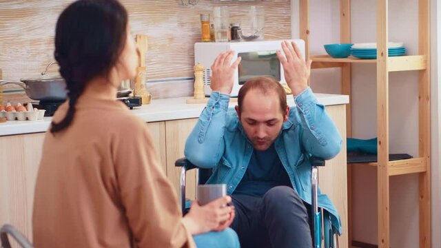 Disabled man in wheelchair having a conflict with wife in kitchen. Guy with paralysis handicap disability handicapped difficulties getting help for mobility from love and relationship