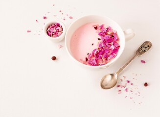 Moon milk with rose petals in a white cup on a light background with space for text. Top view