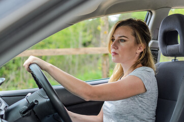 Naklejka premium Young charming girl puts on sunglasses at the wheel of a black car 