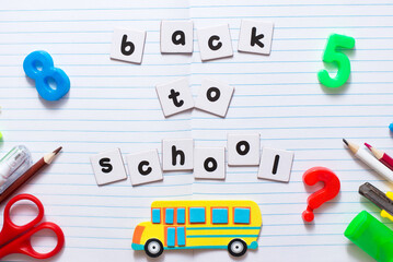 Back to school text on sheet of notebook with colorful school stationery and yellow toy school bus