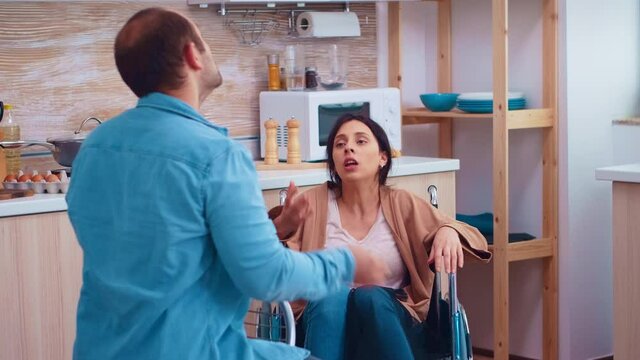 Disabled wife in wheelchair shouting at husband. Couple having a disagreement in kitchen. Woman with paralysis handicap disability handicapped difficulties getting help for mobility from love and