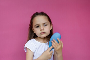 Portrait of a smiling little girl brushing her hair close up on a pink isolated background