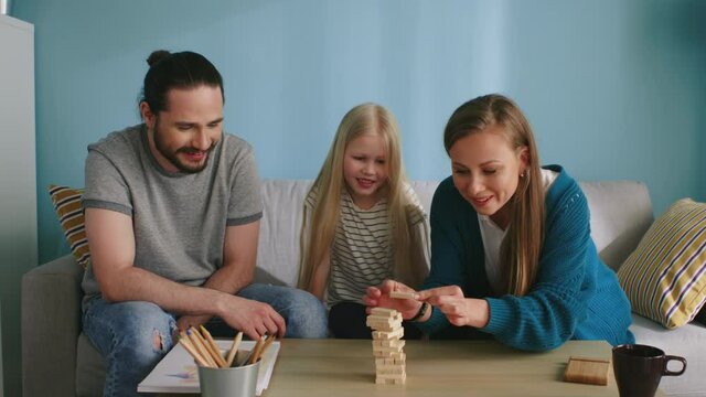 Young family, daughter, mom and dad, have fun together, playing a tiny jenga at home, mom is pulling the bar, all cheer each other, Slow motion.