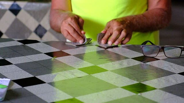 A man in a yellow T-shirt shuffles a deck of playing cards. Tanned hands over the table are warming up before the game. Summer. Georgia. Day.