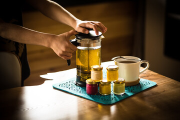 Morning tea with honey. Hands of a boy, a teapot with tea, jars of colored honey with different tastes. Cream honey of red, yellow, green and white color. White tea cup.
