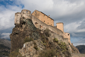 Fototapeta premium Panoramic view of the citadel perched high on a rock hilltop with dramatic cloudy sky in Corte, Corsica, France