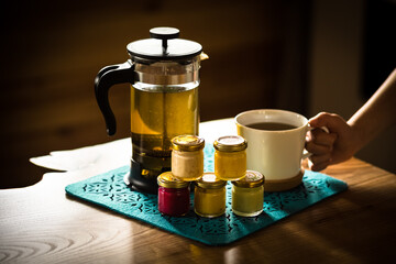 Morning tea with honey. Hands of a boy, a teapot with tea, jars of colored honey with different tastes. Cream honey of red, yellow, green and white color. White tea cup.
