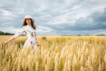 Fototapeta na wymiar Portrait of a girl in a wheat field. Portrait of a beautiful girl in a white dress and hat on a wheat field. Girl in a white dress and hat. Wheat field. Portrait of a young woman in nature