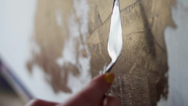 Unrecognizable person drawing with spatula. The hand of a woman artist, holding a spatula for drawing and applying paint to the canvas. Close up footage