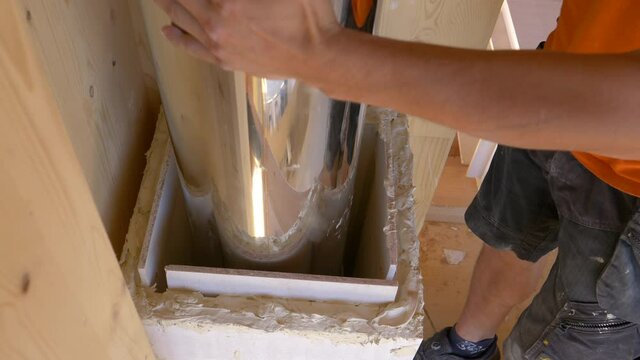 SLOW MOTION, CLOSE UP: Unrecognizable contractor slides a metal chimney pipe down a shaft. Male worker installs a ventilation conduit into a shaft near a wooden wall in an unfinished housing project.