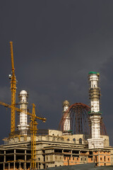 Construction of a mosque. Thunderclouds. The unfinished white mosque shines amid storm clouds. Clouds. Rainbow and Mosque. Crane. Concrete blocks and metal frame. Major construction in the city