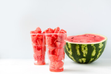 sliced pieces of ripe, juicy, sweet watermelon inside a long, plastic Cup on a light background front view. The concept of light, summer food.