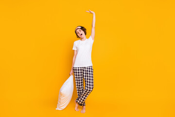 Full length photo of funny lady sleepy morning eyes closed enjoy saturday raise hands up stretching hold pillow wear white t-shirt plaid pajama pants isolated yellow color background