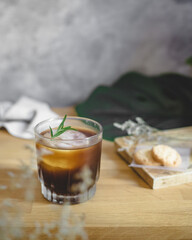 a glass of ice americano coffee with ice ball on concrete coaster and wooden table.