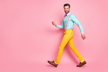 Full size profile side photo of positive guy go walk copyspace use smartphone enjoy leisure time blogging wear shirt bow tie pants shoes isolated over pastel color background