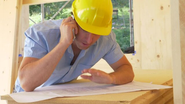 SLOW MOTION, CLOSE UP: Architect is frustrated with builder as they discuss the floor plans over the phone. Caucasian man argues over the phone with architect while examining the house blueprints.