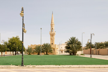 Mosque with minaret in a small place in Saudi Arabia. The lawn in the foreground is artificial turf so that the place looks nicer.