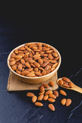 almonds on dark stone table with wood spoon or scoop. Almond in wooden bowl. Nuts freely laid on dark board.