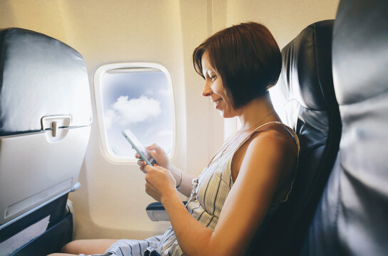 Brunette caucasian woman siting inside aircraft like passenger and taking a picture from smart phone 