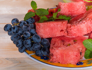 Watermelon, bunch of grapes, mint, on a plate, light wooden table, close-up